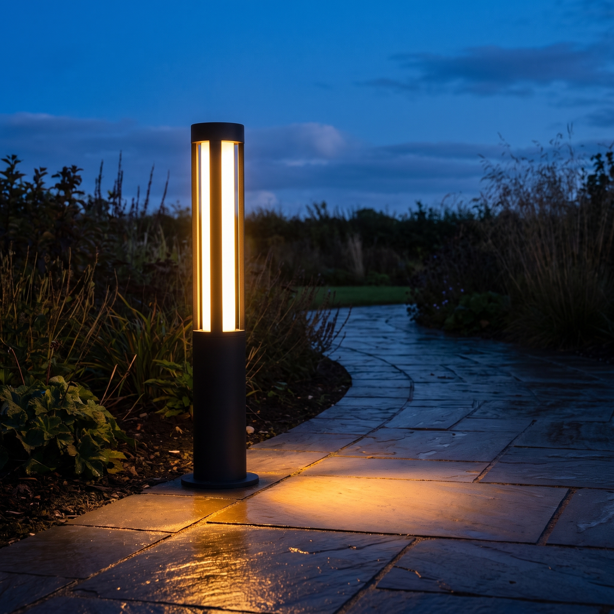 Lumira bollard light glowing warm beside a slate path at dusk