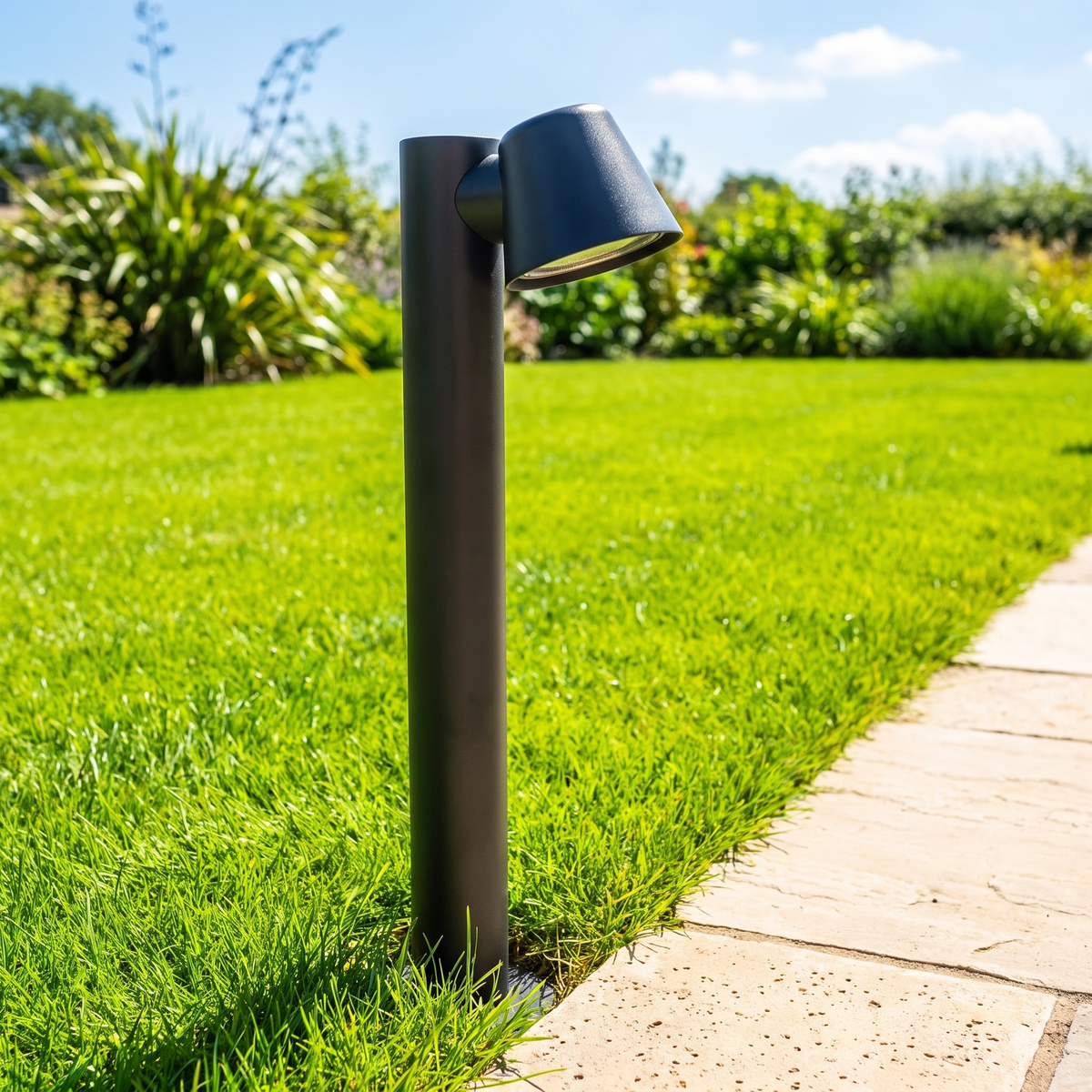 Sentry path light in a bright green lawn beside limestone paving