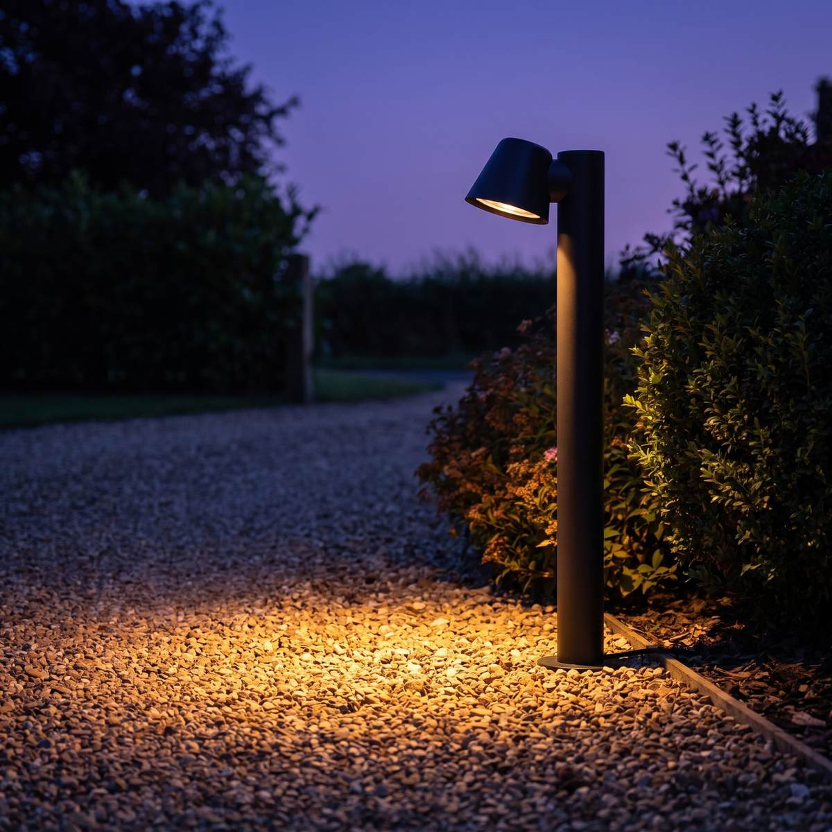 Sentry path light lit at dusk beside a gravel driveway